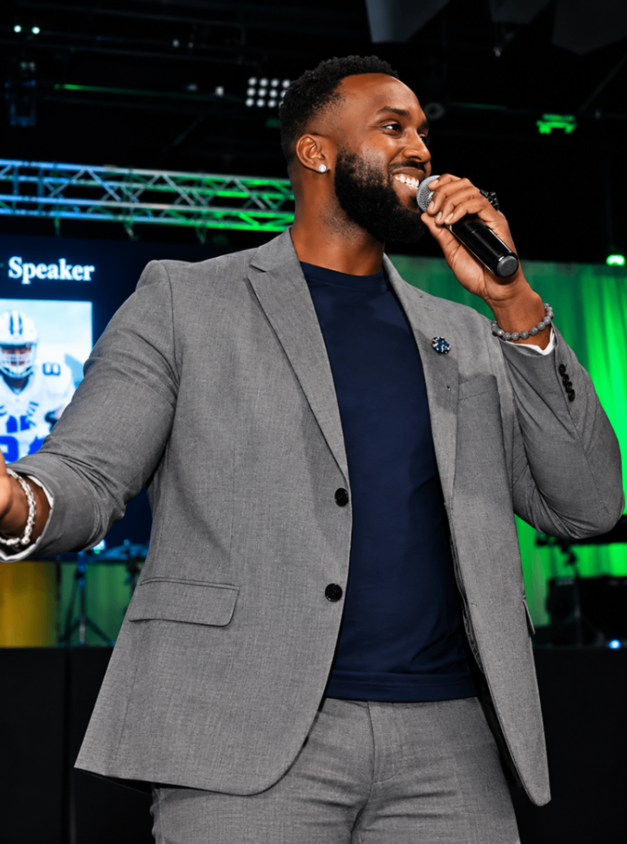 Tony Hills smiling while speaking on stage with a microphone.